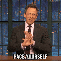A man in a suit gestures with his hands while saying "PACE YOURSELF" in bold text. He is seated at a desk, likely on a talk show set, offering lighthearted advice or a humorous reminder to take things slow. The GIF conveys a message of moderation or patience.