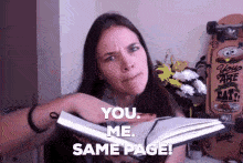 A woman holds an open book, gesturing emphatically as she says, "You. Me. Same page!" Her expression is serious but slightly humorous, emphasizing the need for alignment or mutual understanding. The tone is playful, suggesting she’s trying to make sure everyone is in agreement or on the same wavelength.